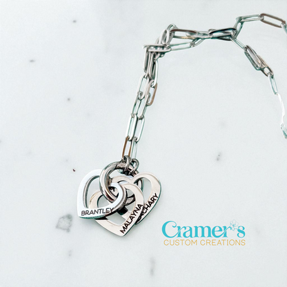 Silver bracelet with interlocking heart charms on a light gray background, featuring 'Cramer's Custom Creations' logo.