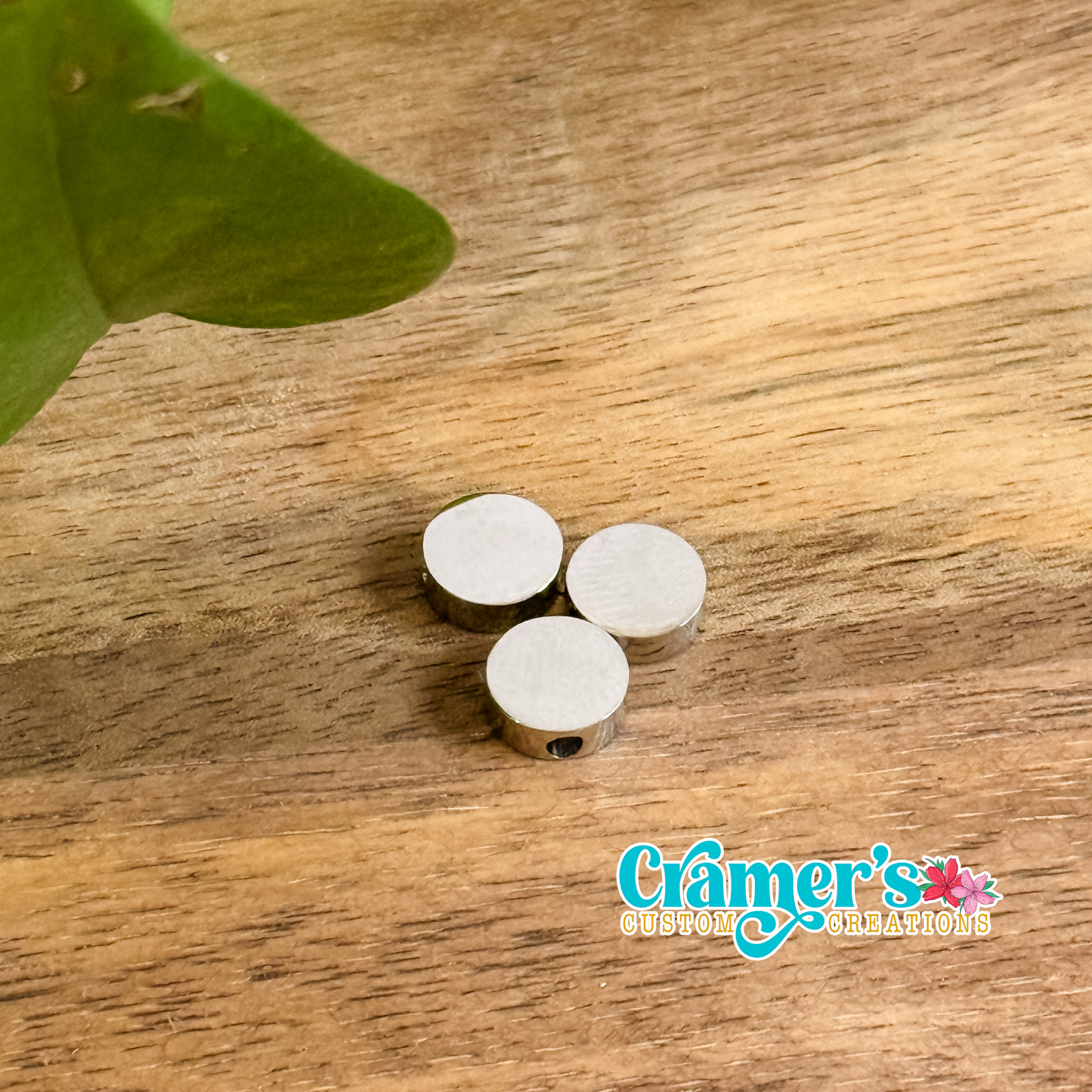 Three circular pendants on a wooden surface, with one silver and two gold colored, from Cramer's Custom Creations.