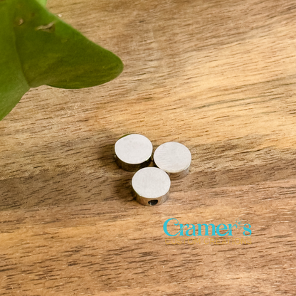 Three circular pendants on a wooden surface, with one silver and two gold colored, from Cramer's Custom Creations.