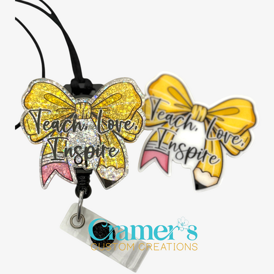 2 badge reels showing a glitter and a non glitter option of a badge with the words teach love inspire on a bow colored like a pencil