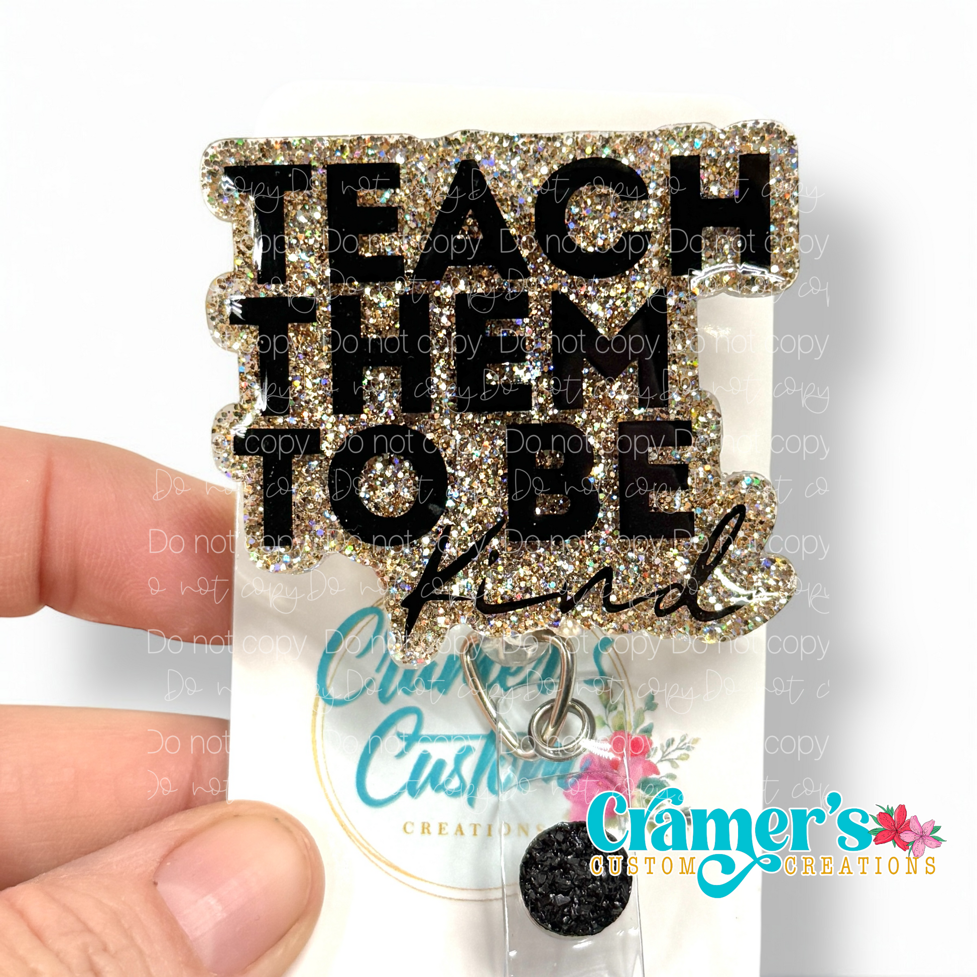 badge reel showing a gold glitter background with teach them to be kind in black