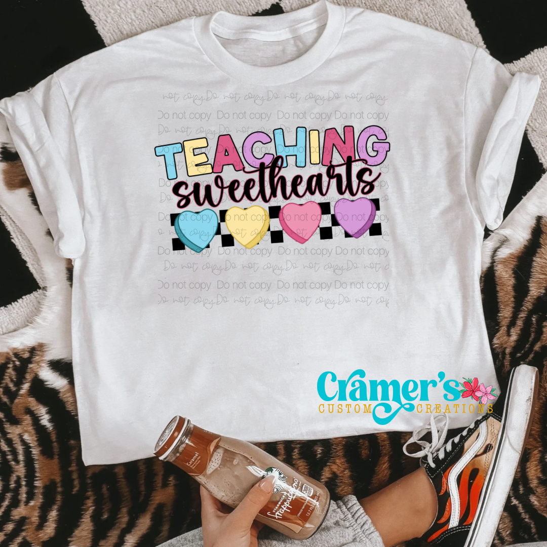 a flat lay of a white shirt with multi color design saying teaching sweethearts with heart shapes