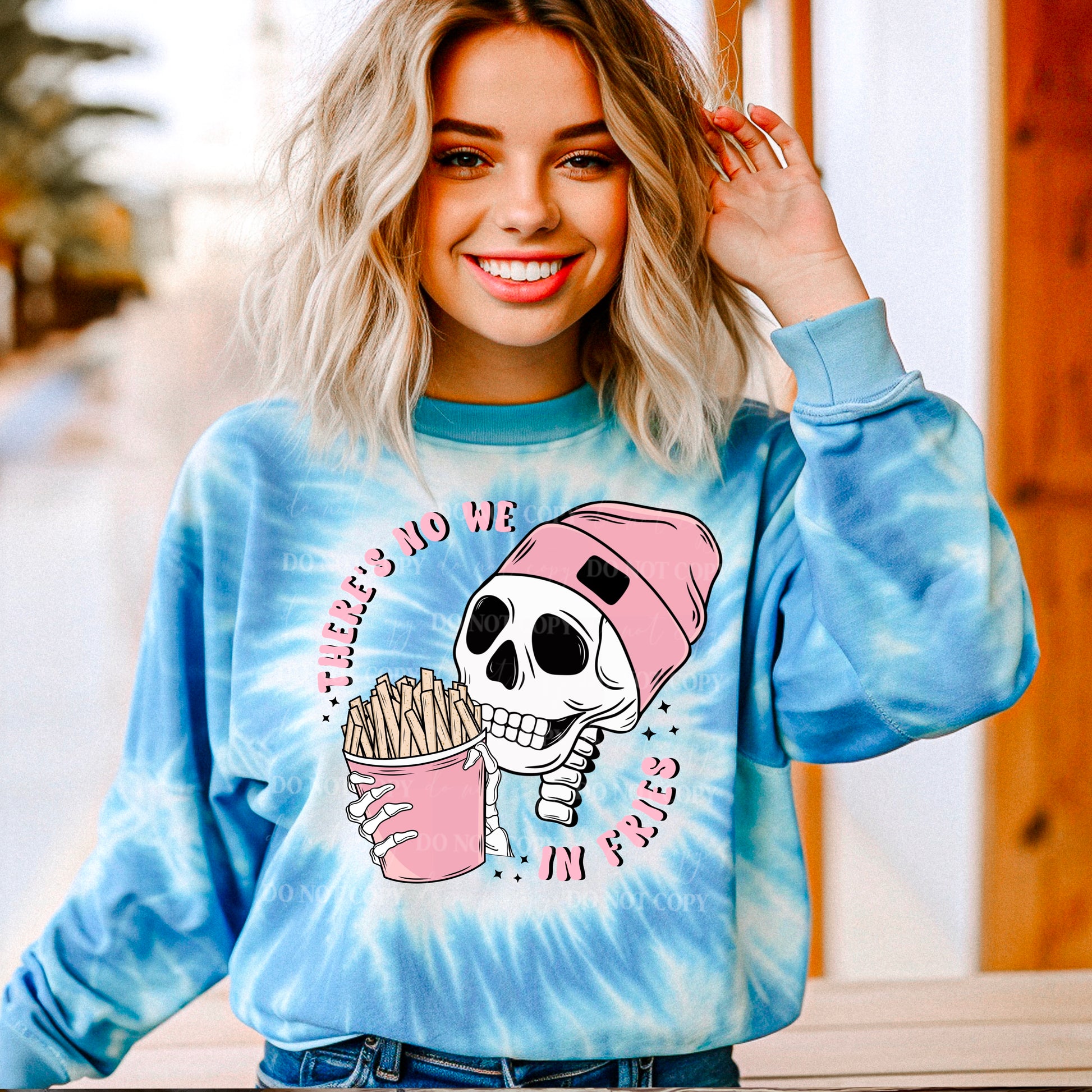 A person wearing a blue tie-dye sweatshirt with a graphic print of a skull holding a pink cup and the text 'There's no WE in Fries'.