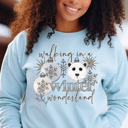 woman wearing a light blue sweatshirt with the quote walking in a winter wonderland.  the shirt has ornaments, a bear and snowflakes 