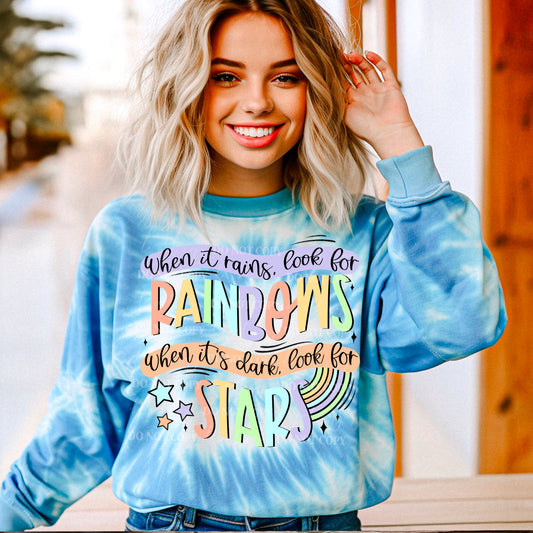 A person wearing a tie-dye sweatshirt with text design looking towards the camera and smiling.