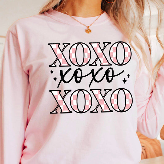 girl wearing a pink sweatshirt that has xoxo across it three times with pink check in the letters