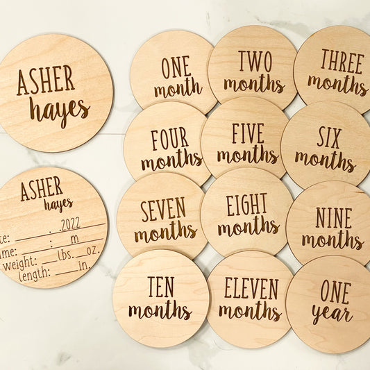 Multiple wood discs engraved with names, stats, and birth month markers on a white background