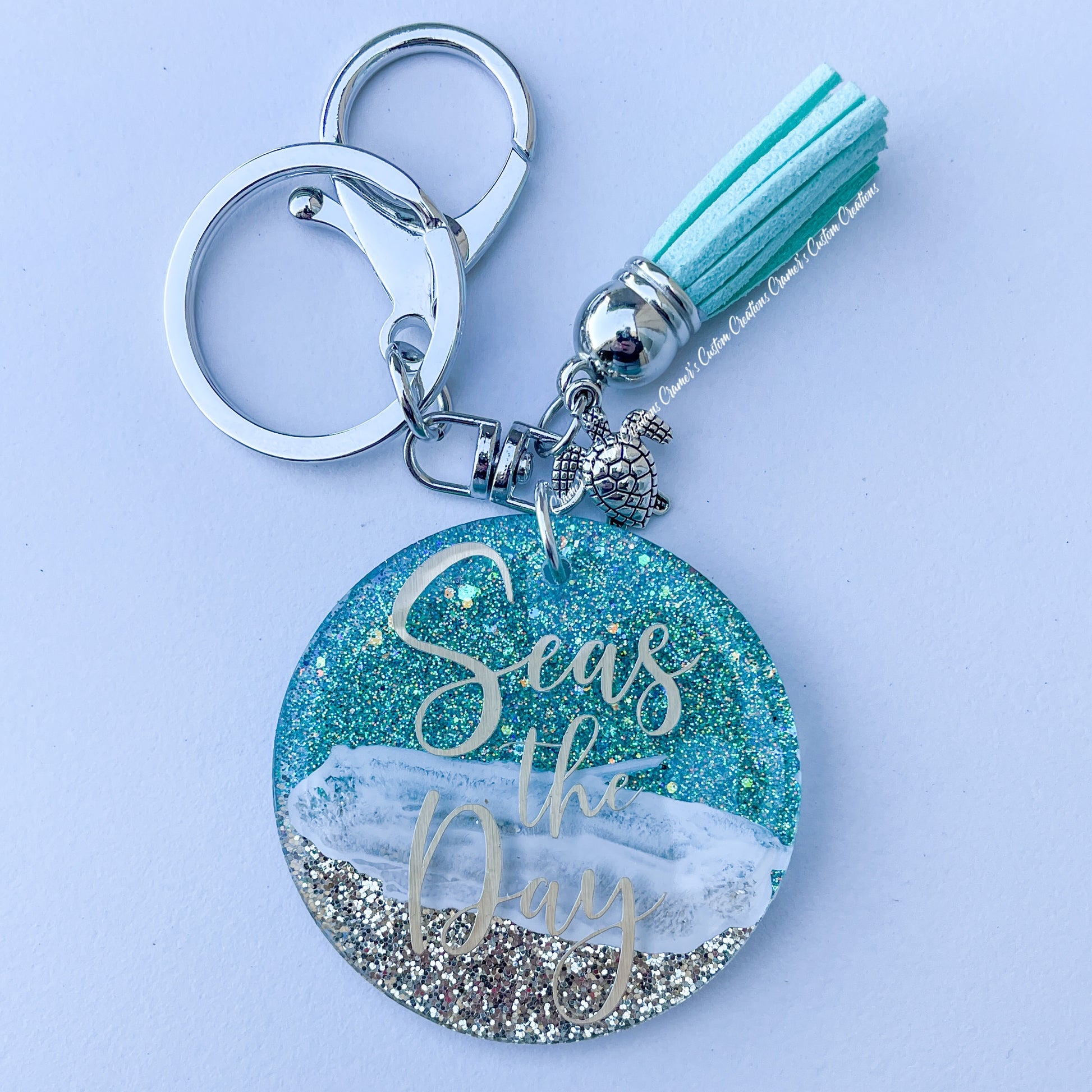 a keychain with beach colors saying seas the day on a white background.  the keychain has a teal tassle and a sea turtle along with a lobster claw
