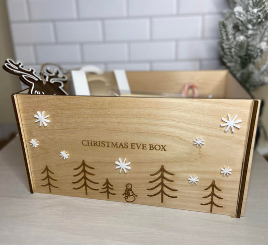 A wooden gift box with 'Christmas Eve Box' text, decorated with pine trees and snowflake designs.