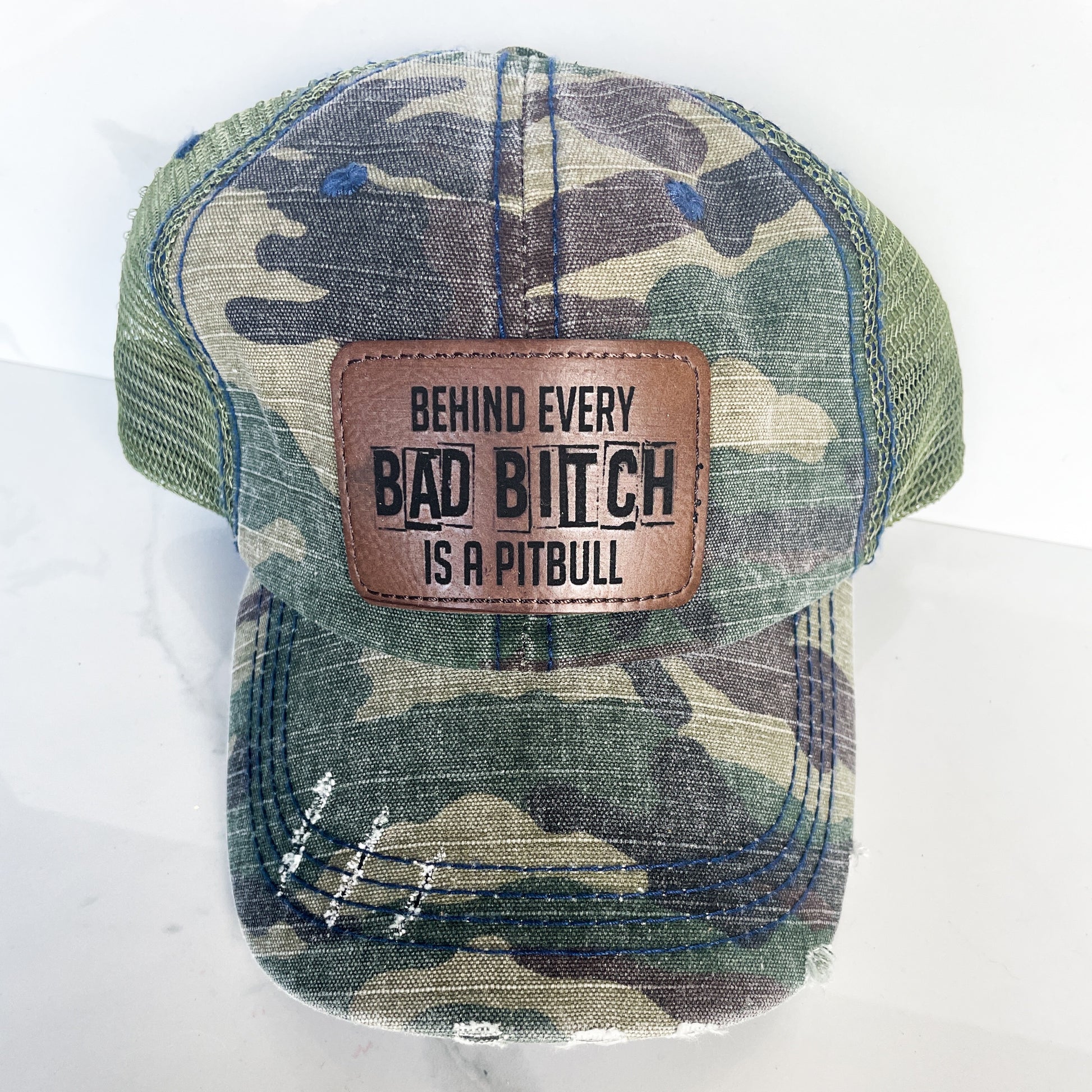 a camo unstructured hat with a rawhide colored patch on the front with behind every bad bitch is a pitbull