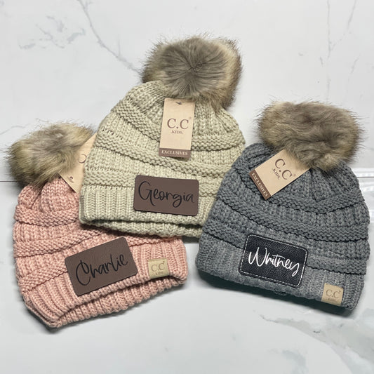 three pom pom beanies  personalized with charlie, georgia, and whitney names on them with a white background