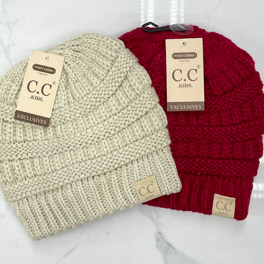 Two kids' hats, one beige and one red, each with a leather patch on the front that reads 'CC Kids'.