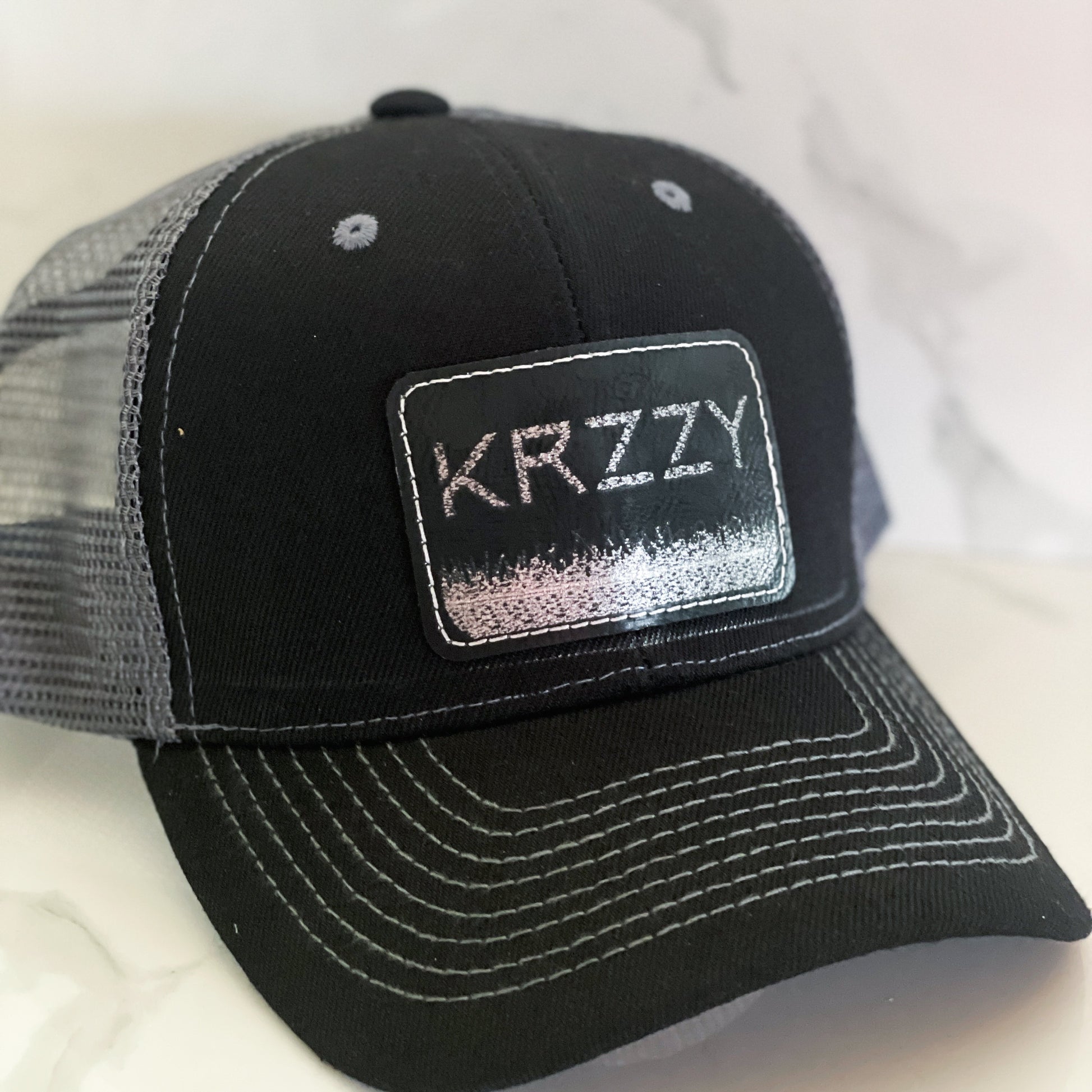 A black hat with a personalized leather patch on the front that reads 'KRYZZY'.