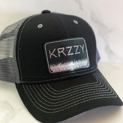 A black hat with a personalized leather patch on the front that reads 'KRYZZY'.