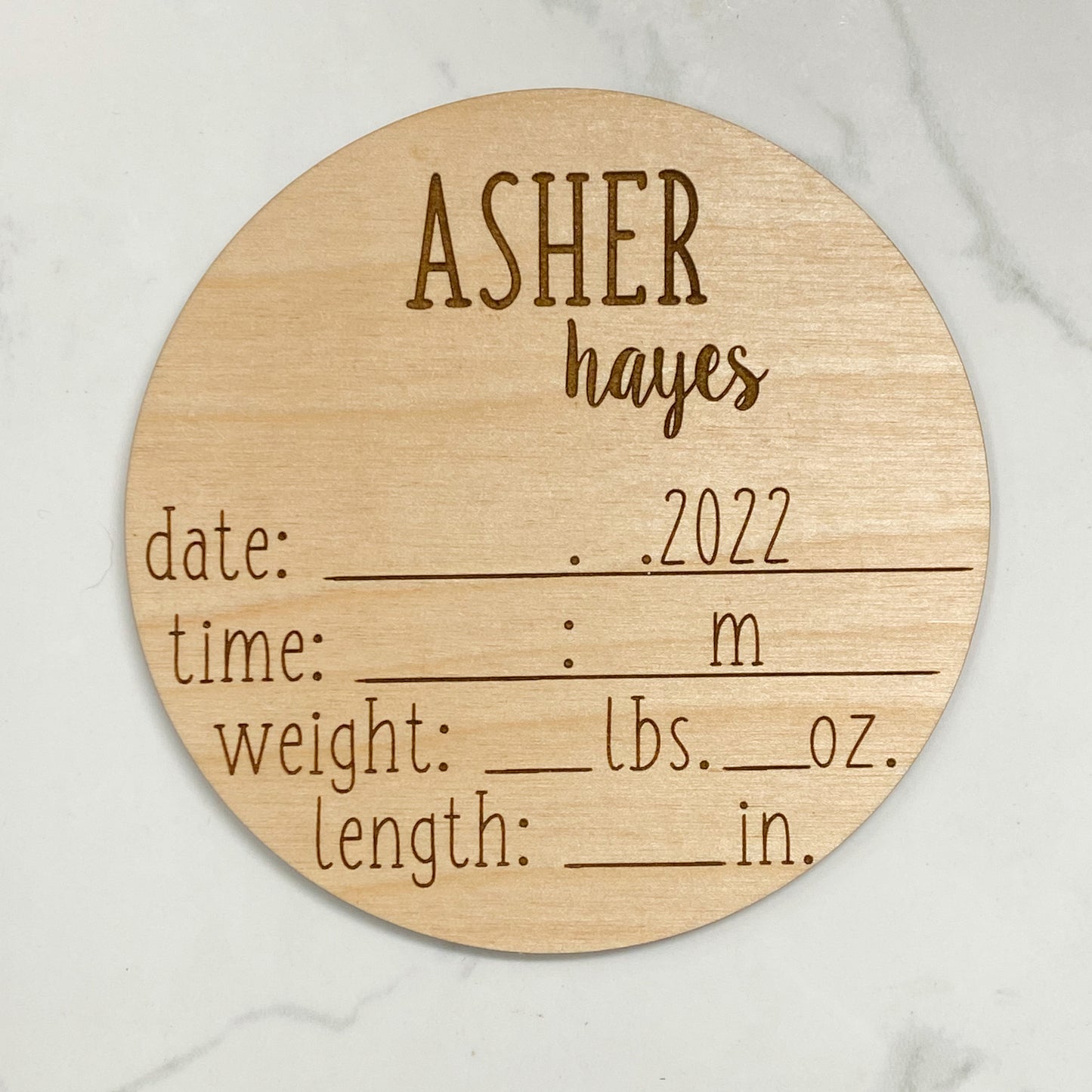 a wood disc showing a childs name and all birth stats engraved with blank spaces to write the info in. its on a white background