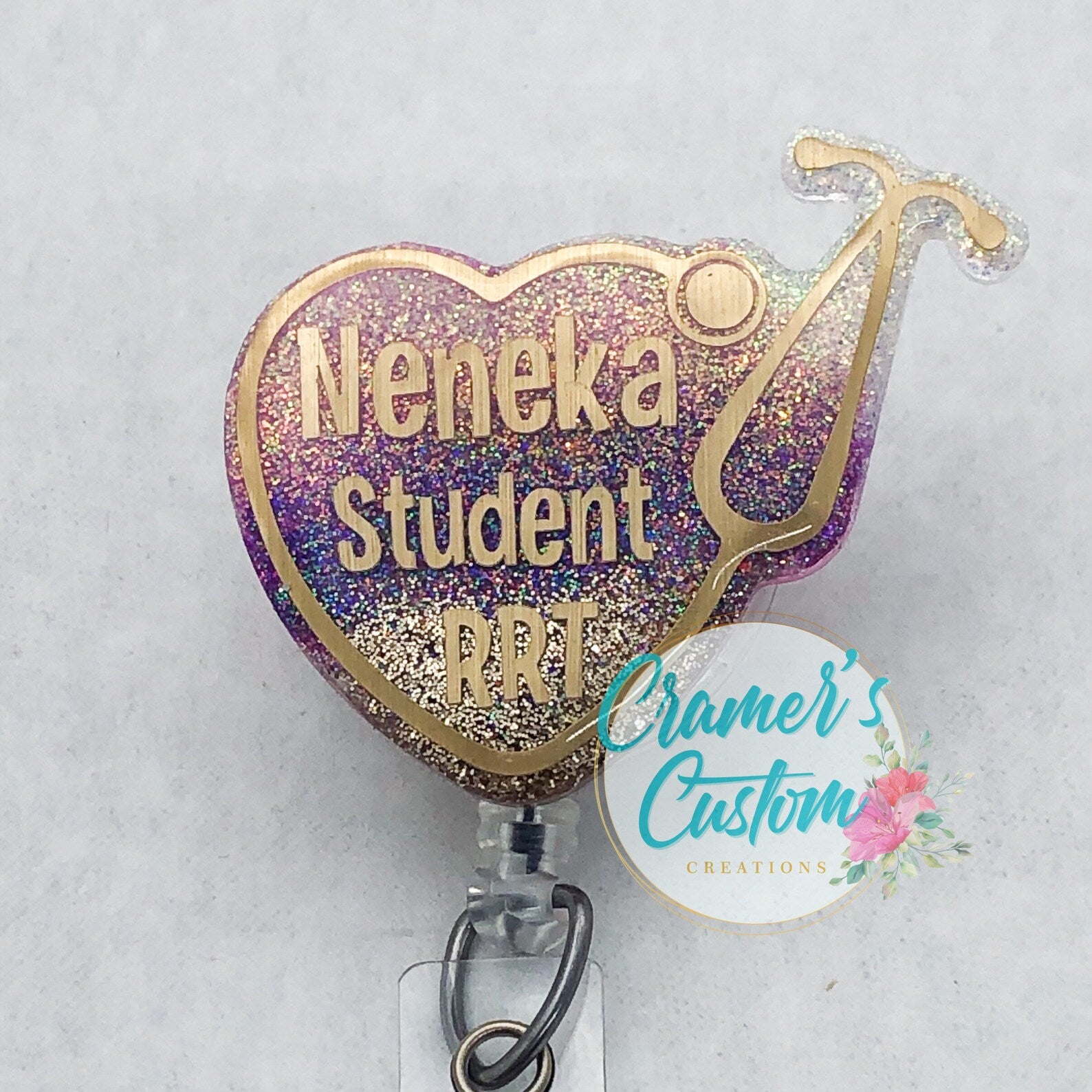 a stethoscope heart badge reel with gold writing and a hold stethoscope, with the glitter being a wine, pink, gold ombre, on a  white background